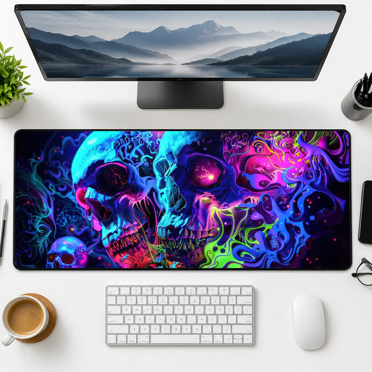 Top-down view of a clean modern desk setup with a widescreen monitor showing a mountain landscape, an extended neon skull psychedelic mouse pad, white keyboard and mouse, coffee cup, plant, and office supplies neatly arranged
